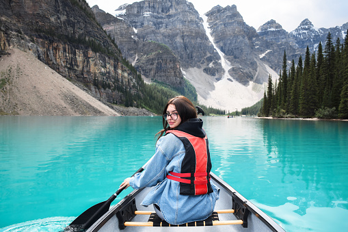 Young girl looking back over shoulder while riding in canoe on turquoise blue Moraine lake with view of mountains