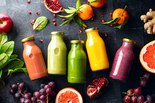 Various colourful fresh raw ingredients and already blended mix in a bottles for individual consumption are on the kitchen table surface. Top down view composition.