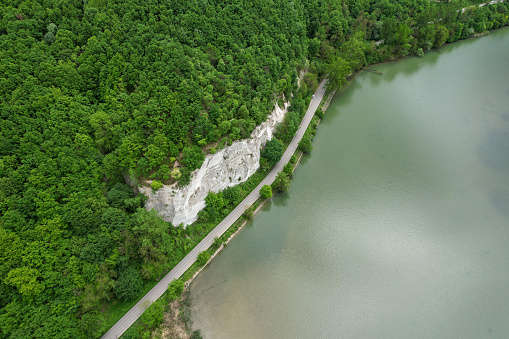 An asphalt road winding along a lake's water edge. Hardwood forests are growing near the lake and on top of an abrupt cliff. Carpathia, Romania.