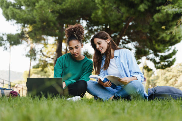 due studentesse che lavorano e imparano insieme sedute sull'erba del campus universitario - college student high school student education learning foto e immagini stock