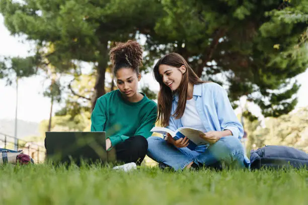 Photo of Two female students working and learning together sitting on University campus grass