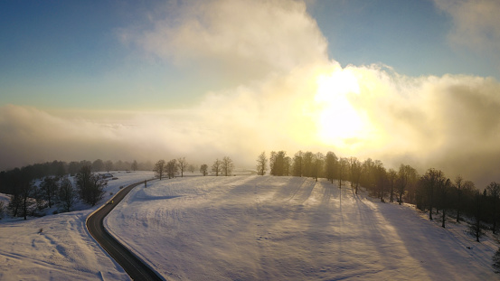 Aerial drone flight between clouds during winter season. A pale sun shines above the clouds after a cold and snowy blizzard. Sunset time. Carpathia, Romania