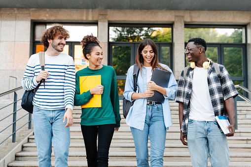 Estudiantes felices caminando juntos en el campus universitario, charlando y riendo al aire libre después de clases photo