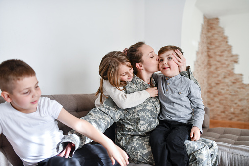 Caring Mother In Military Uniform Embracing And Kissing Children