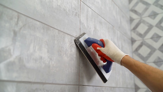 Tile grout. Construction work with ceramic tiles. Grouting, joining wall tiles. The builder processes the seams between ceramic tiles. Seam grouting with black grout.