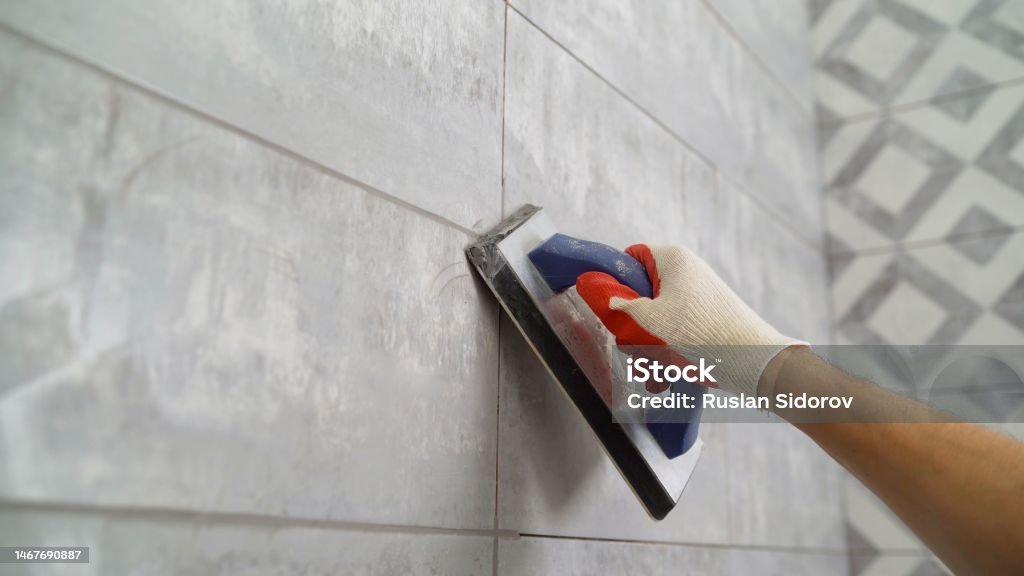Tile grout. Construction work with ceramic tiles. Grouting, joining wall tiles. The builder processes the seams between ceramic tiles. Seam grouting with black grout. Seam grouting with black grout. Tile grout. Construction work with ceramic tiles. Grouting, joining wall tiles. The builder processes the seams between ceramic tiles. Grout Stock Photo