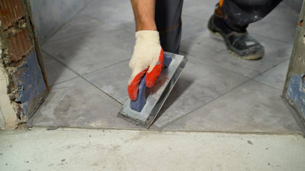 Man grouting the joints between the tiles with a sponge. The hand of man holding a rubber float and filling joints with grout. The worker rubs the seams on the floor, ceramic tiles. stock photo
