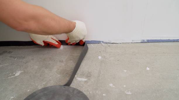 The man glues a damping tape on a wall bottom, protection for a floor coupler. The damping tape is glued to the floor. Gluing the tape to the junction of the wall and the floor, for pouring the floor. Damper tape. stock photo