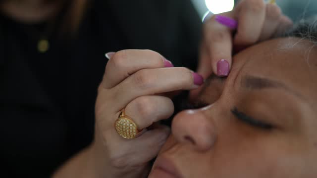 Close-up of a beautician tweezing a woman's eyebrows at a beauty salon