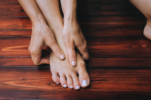 A two woman's hand massages her own foot. The concept of leg fatigue, spasms, cramps. Hygiene and health.