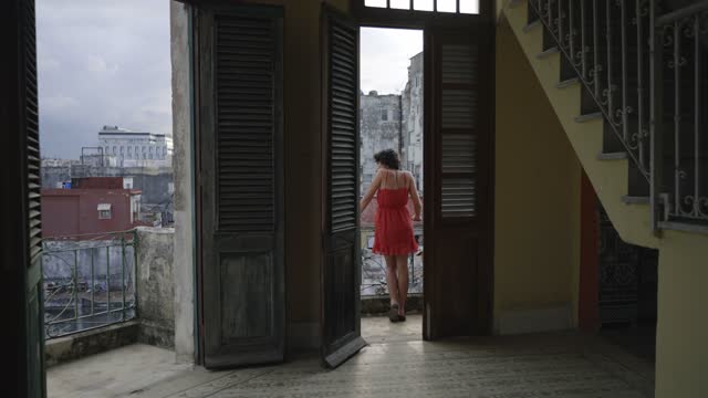 Young Hispanic woman with a red dress contemplating city from balcony at old colonial attic loft