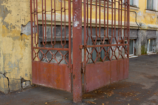 Red metal wrought-iron gates on the background of an old yellow building. Cracked over time. Entrance to the courtyard.