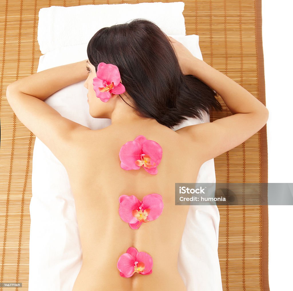 Attractive Woman Relaxing Spa with Flowers Attractive young woman relaxing in spa, beauty, wellness salon laying on the bamboo mat Adult Stock Photo