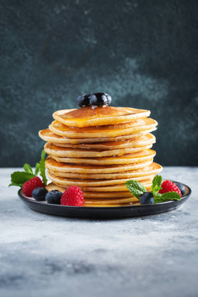 istock Delicious pancakes, with fresh blueberries, raspberry and maple syrup or honey on a dark background 1467713661