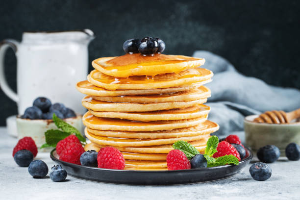 istock Delicious pancakes, with fresh blueberries, raspberry and maple syrup or honey on a dark background 1467713664