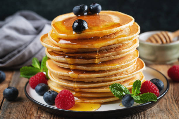 istock Delicious pancakes, with fresh blueberries, raspberry and maple syrup or honey on a dark background 1467713682