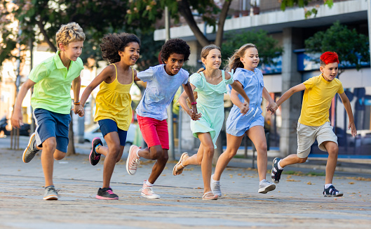 Group of cheerful tweenagers of different nationalities running together along city street on summer day. Happy healthy kids concept