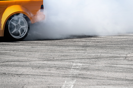 closeup side view of yellow sport car drifting on gray speed tarmac track with white smoke coming out of the back tire wheel with copy space available