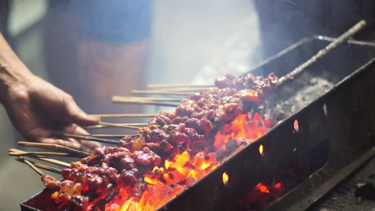 Goat satay on traditional charcoal fire. satay on fire with smoke and an appetizing look. hands cooking satay on the grill