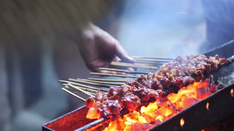 Goat satay on traditional charcoal fire. satay on fire with smoke and an appetizing look. hands cooking satay on the grill