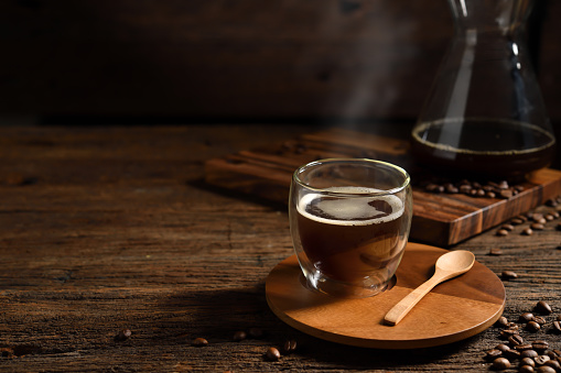 Cup of drip coffee with smoke and coffee beans on old wooden background