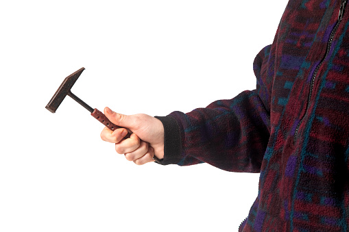 woman hand holding hammer. Isolated background. Studio shoot. A woman is holding an old hammer. The woman's face is not visible. He has a purple coat on. Close-up.