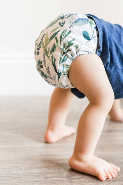 istock A 1-Year-Old Baby Boy Playing on the Floor & Learning to Walk While Wearing Just a Cloth Diaper With a Leaf Pattern & a Blue Shirt 1467743961