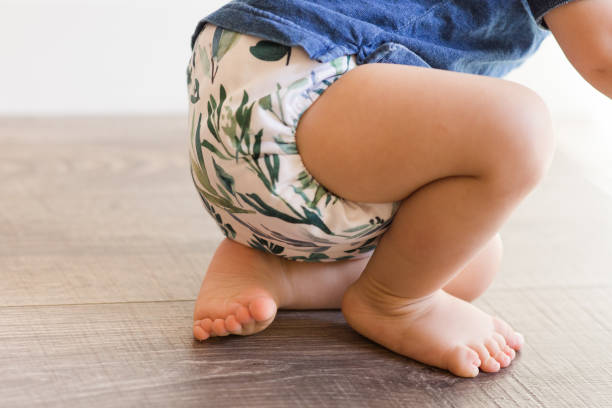 A 1-Year-Old Baby Boy Playing on the Floor & Learning to Walk While Wearing Just a Cloth Diaper With a Leaf Pattern & a Blue Shirt