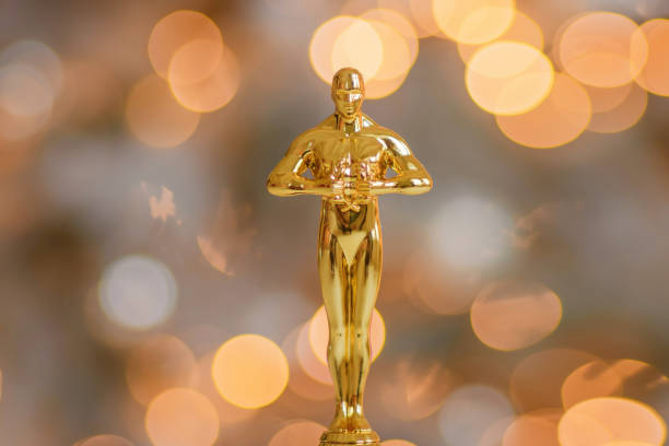 Golden award statue replica at bokeh garland lights background Hollywood gold oscars trophy figurine imitation seen during an award cinema ceremony. Success and victory concept close up statuette at twinkle yellow lights background soundtrack stock pictures, royalty-free photos & images