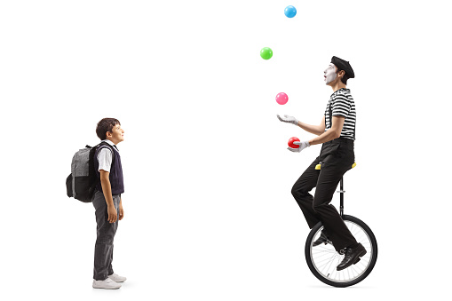 Full length shot of a schoolboy looking at a mime juggling and riding a unicycle isolated on white background