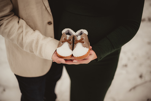 A pregnant couple holding baby boots in their hands