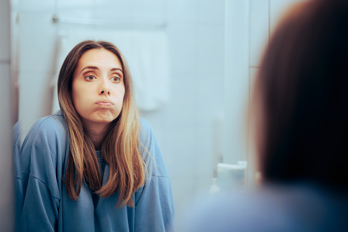 Mujer infeliz mirándose en el espejo sintiéndose abrumada photo