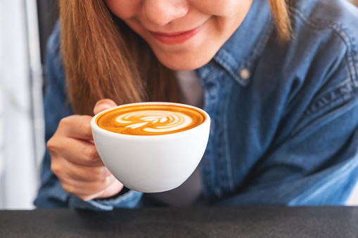 Closeup image of a young woman holding and drinking hot latte coffee