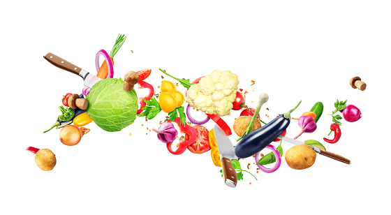Kitchen knives are flying through and cutting wave of vegetables on a white background
