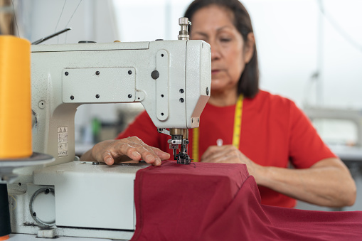 Selective focus on a sewing machine in a workshop while a mature hispanic woman is working