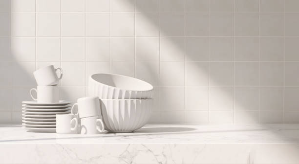 istock Clean, minimal white marble kitchen countertop with stack of ceramic coffee cup, saucer, bowl in sunlight from window on white square tile wall 1467775477
