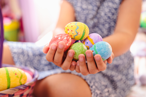 Unrecognizable latin girl holding handful of colorful painted easter eggs in her bedroom. Christian holiday