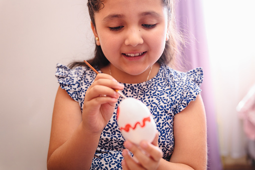 Close up of a smiling cute latin girl painting easter eggs in her bedroom. Easter holiday from the perspective of a child.