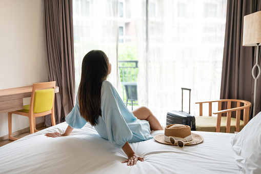 Carefree young Asian traveler woman relax on bed in hotel room. Travel alone, summer weekend concept.