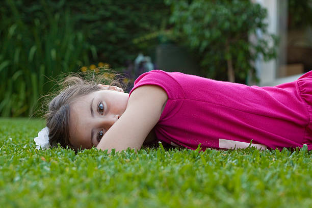 NiAa of 6 years lying on the green spring grass. has a fuxia t-shirt and looks straight ahead