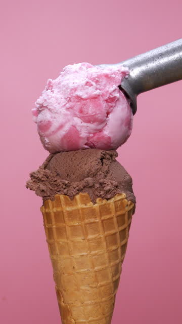 Vertical video front view, Scoop of strawberry ice cream on top of chocolate ice cream cone on pink background.