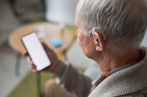 Rear view of senior man with gray hair with hearing aid watching video on his smartphone