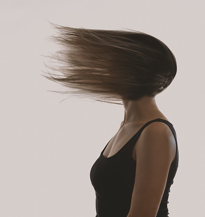 Beauty and fashion concept. Abstract woman portrait with blowing hair on face. model face totally covered with long hair. Image contain motion blur and grain
