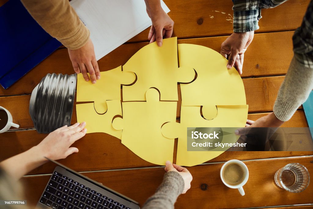 Creating ideas in team! Above view of unrecognizable creative team cooperation while making light bubble of puzzles at casual office. Teamwork Stock Photo