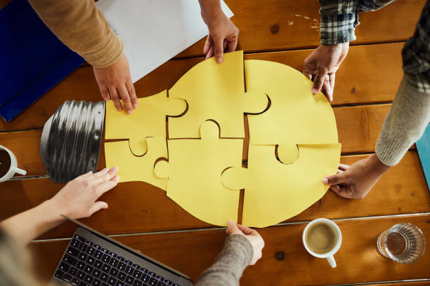 Creating ideas in team! Above view of unrecognizable creative team cooperation while making light bubble of puzzles at casual office. approach stock pictures, royalty-free photos & images