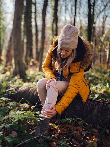 Young female hiker holding her ankle in pain during autumn day in the forest. Photographed in medium format.