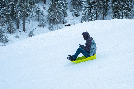 A man on a sled rolls down a snow-covered mountain. Outdoor fun on weekends.