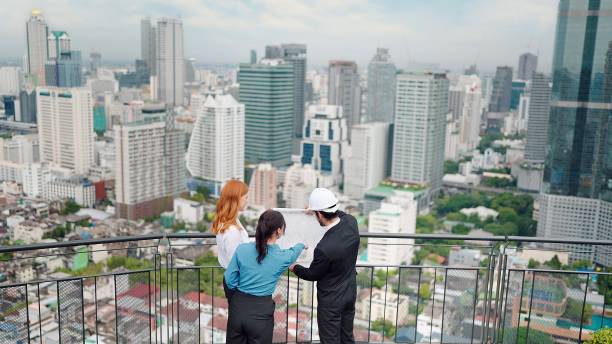 istock Back view of group business people standing looking plans for building construction at rooftop and city view 1467806100