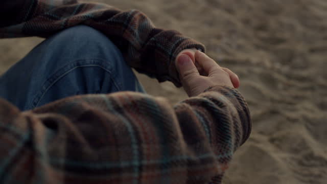Unrecognizable man sitting on sandy beach alone. Closeup guy clasped hands