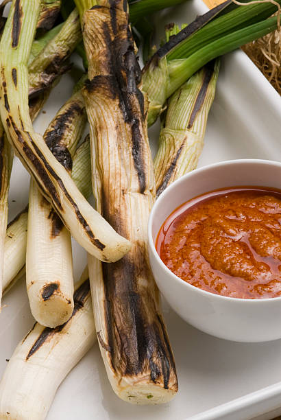 Grilled spring onions in romesco sauce. Spanish cuisine. Calçots. stock photo